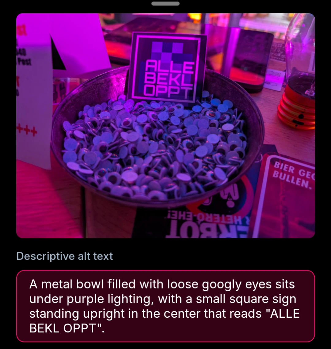 A metal bowl filled with loose googly eyes sits under purple lighting, with a small square sign standing upright in the center that reads "ALLE BEKL OPPT".