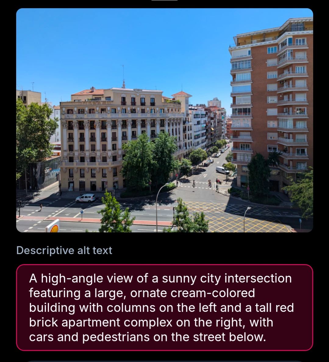A high-angle view of a sunny city intersection featuring a large, ornate cream-colored building with columns on the left and a tall red brick apartment complex on the right, with cars and pedestrians on the street below.