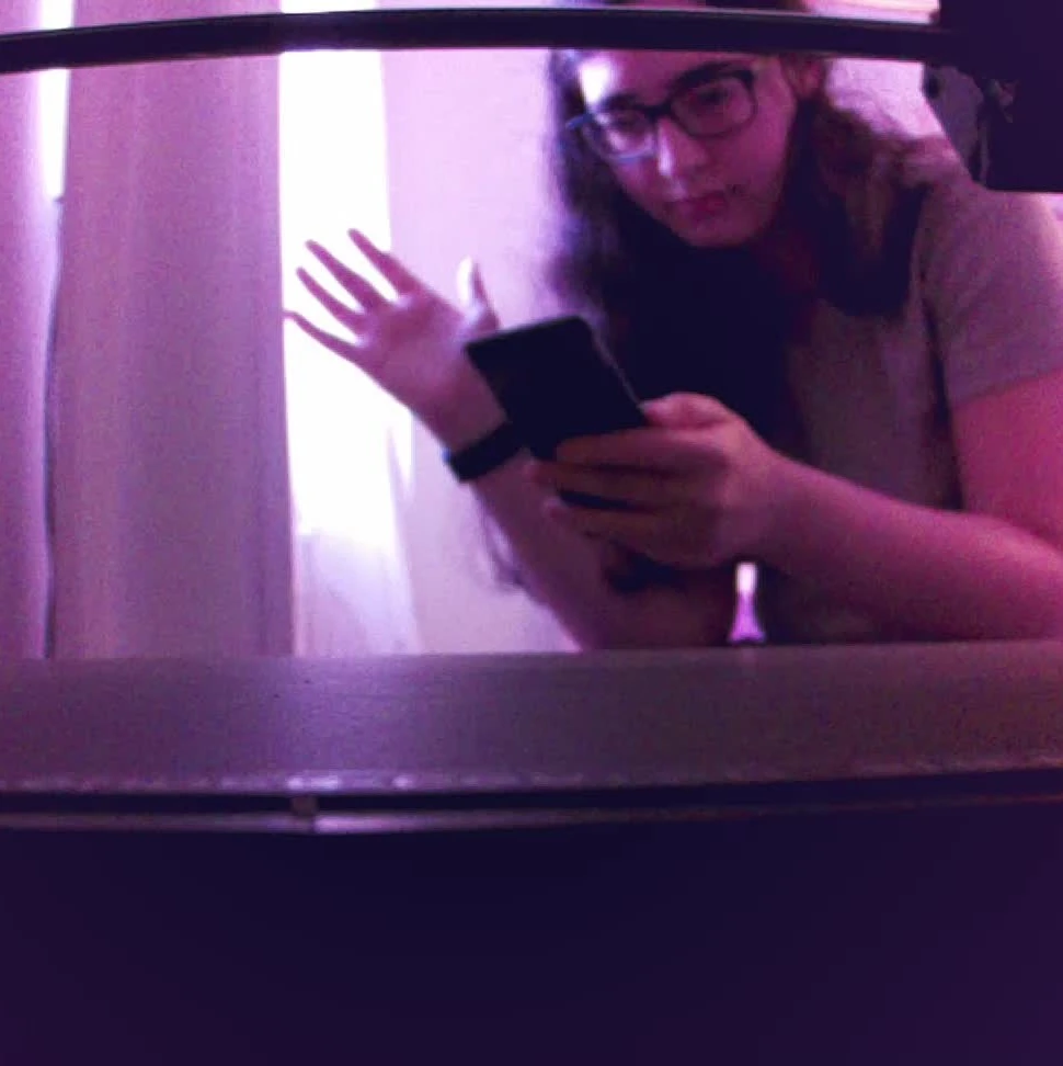 a picture of me taken through an IR camera with a rather wide angle, there's a pinkish/purplish tint to everything, I'm waving at the camera, the view is primarily looking at a 3d printer